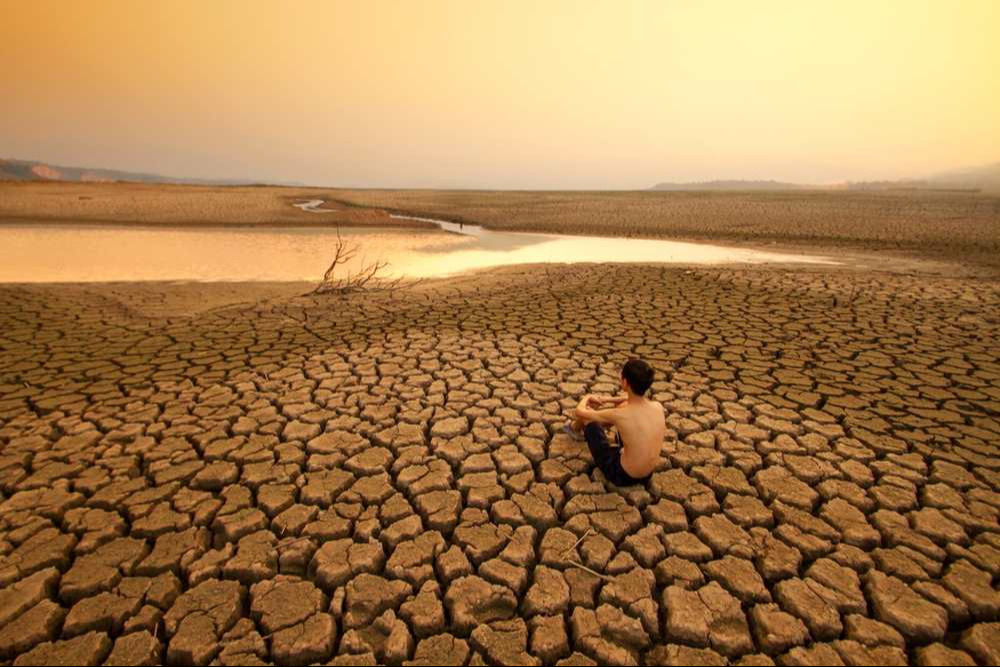 Young man sit on dry cracked earth near drying river or lake metaphor Water crisis, Drought and climate change. Young man sit on dry cracked earth near drying river or lake metaphor Water crisis, Drought and climate change.